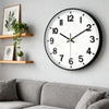 A round black wall clock with white face and black hands hangs on a gray wall above a sofa.