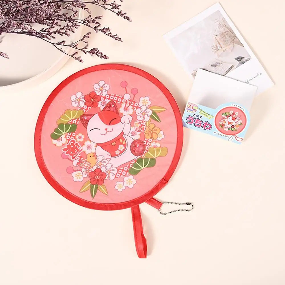 A pink fabric fan with a floral design and a white card is shown on a light background.