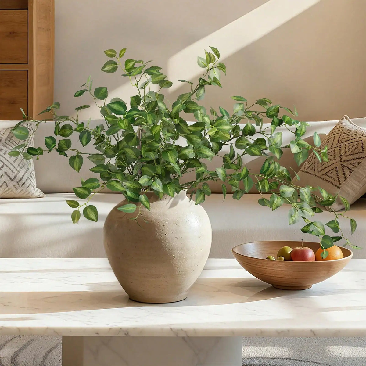 A potted artificial eucalyptus stem with silk greenery branches sits on a marble table.