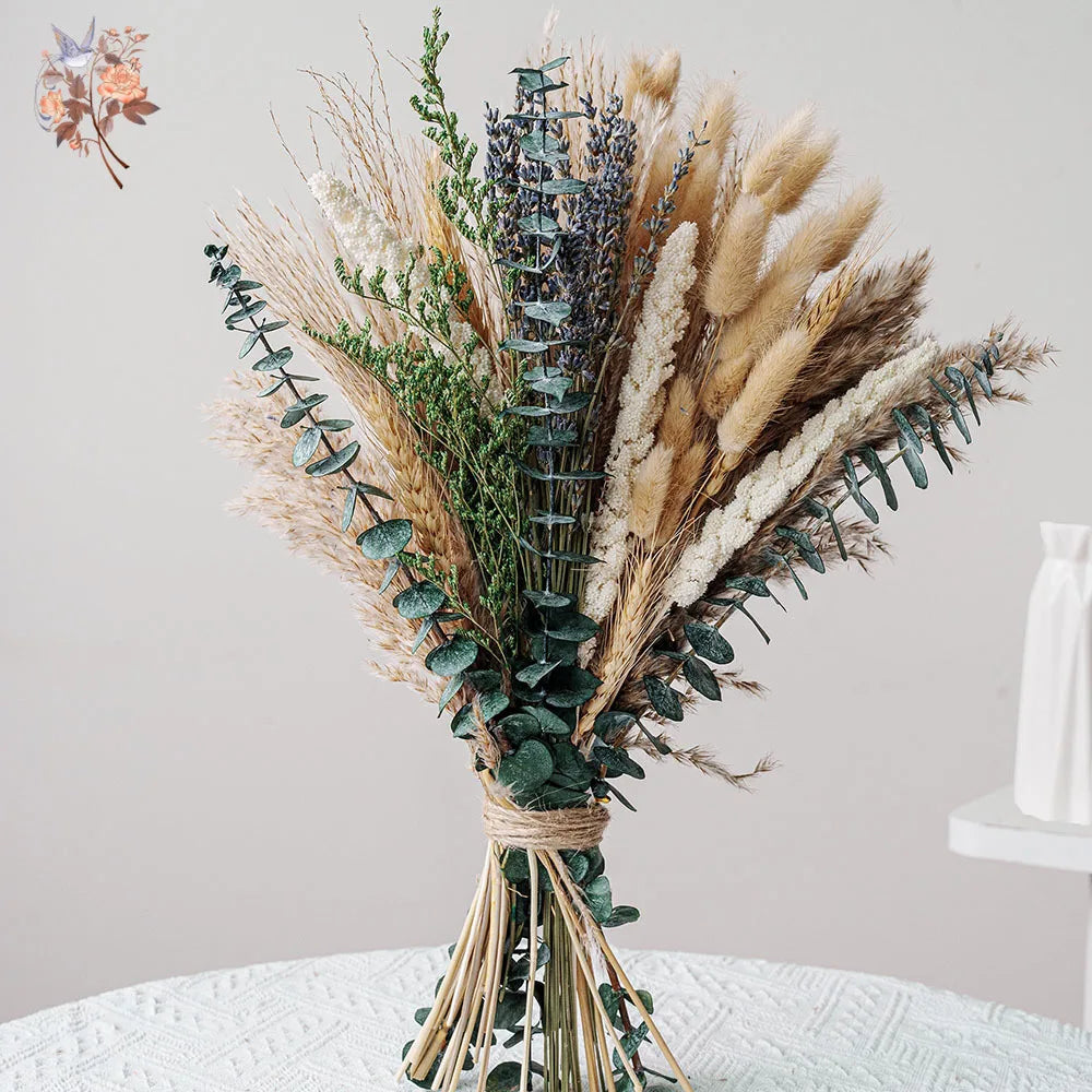 A dried flower bouquet featuring various textures of beige, green, and purple grasses and eucalyptus foliage.