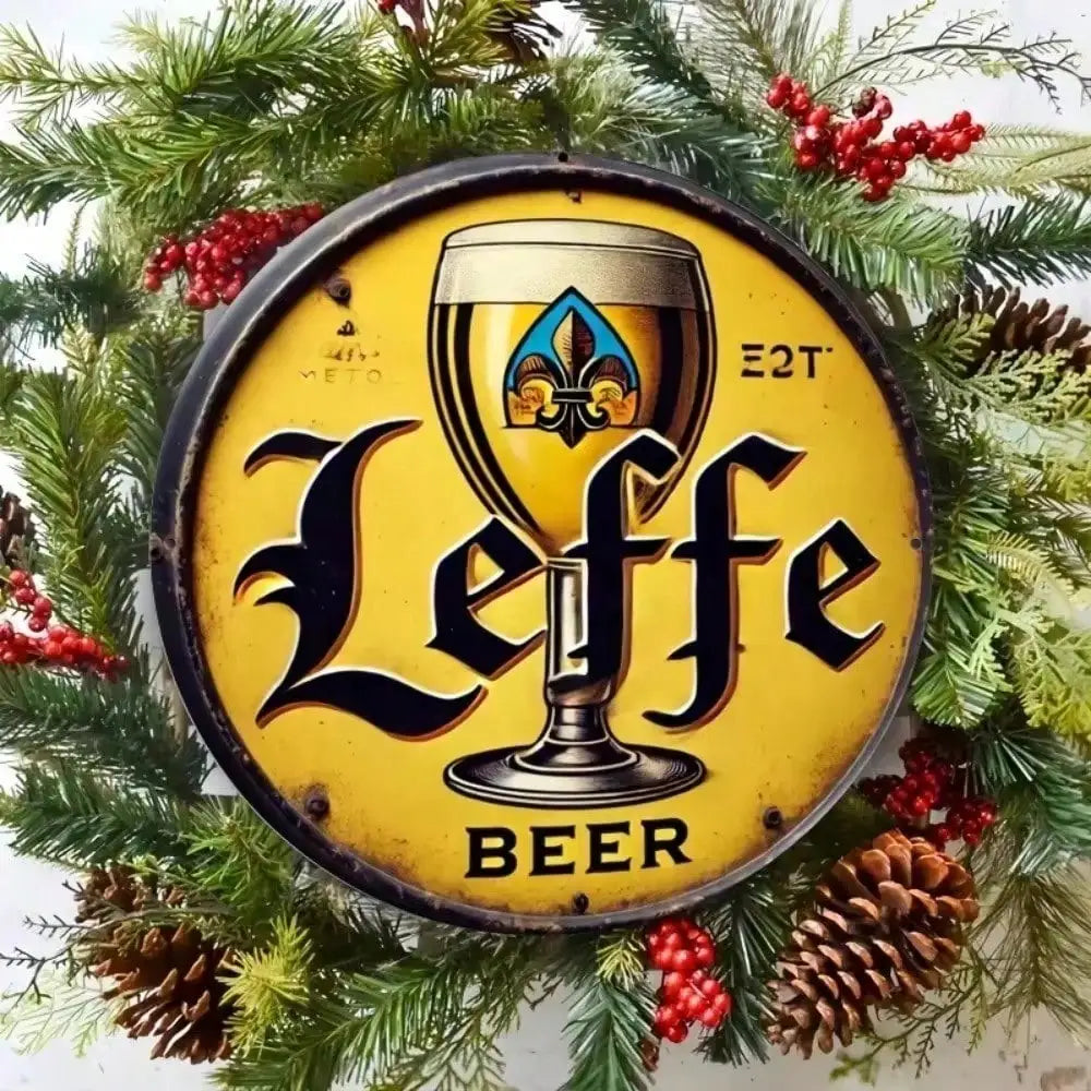 A vintage metal tin sign for Leffe Beer with a black silhouette of a beer glass on a yellow background, decorated with evergr