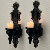 A set of two vintage wrought iron wall-mounted candle holders with black bases and lit candles.