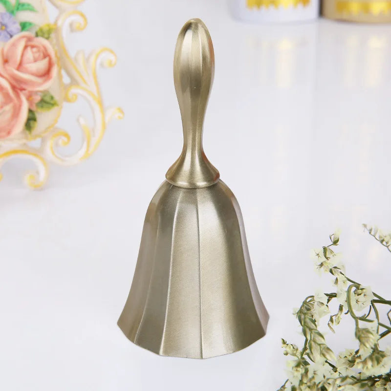 A polished brass hand call bell with a flared, conical shape resting on a white surface.