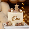 A round cake decorated with a golden 'One' topper and various brown and white teddy bear-shaped edible toppers.