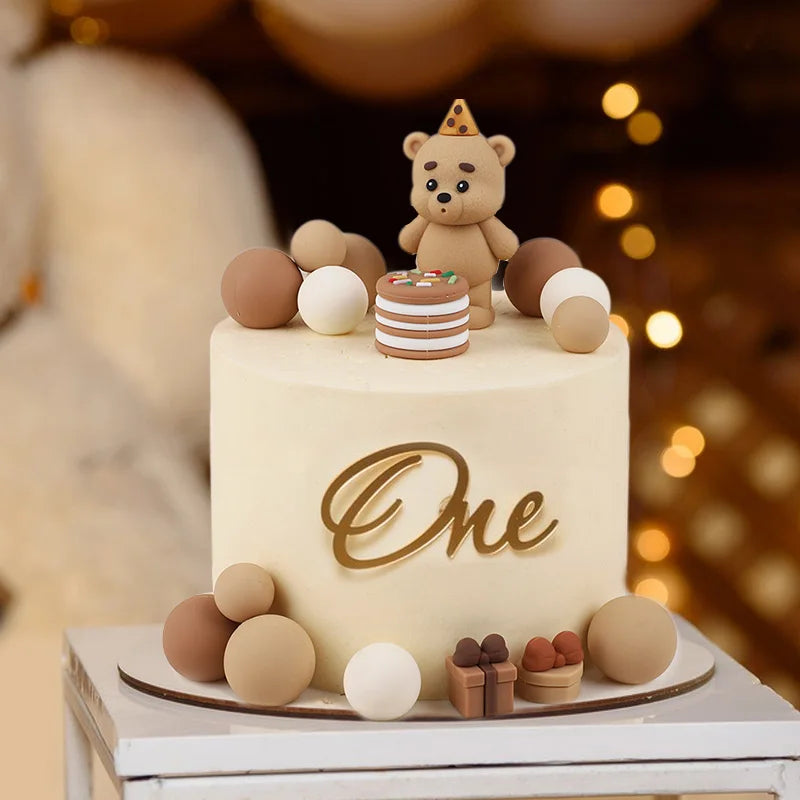 A round cake decorated with a golden 'One' topper and various brown and white teddy bear-shaped edible toppers.