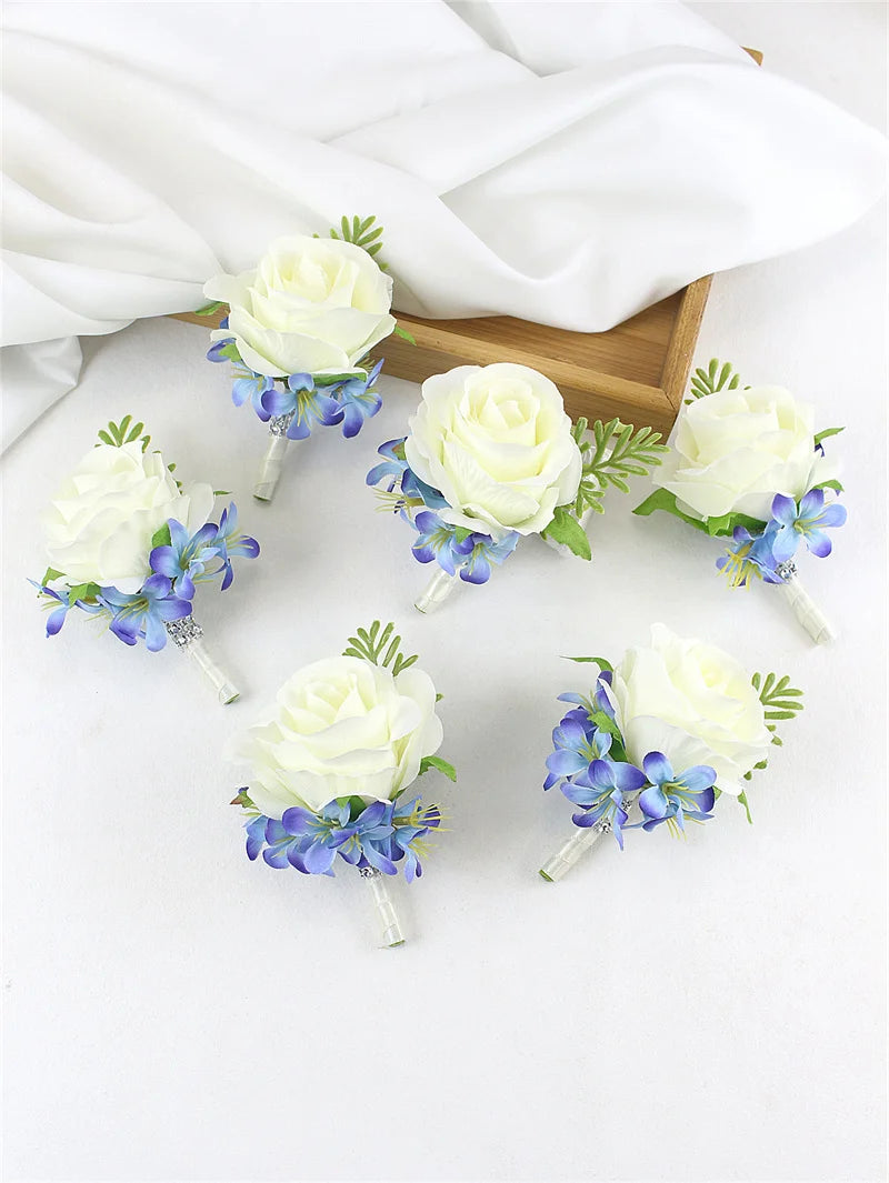 A set of six silk rose boutonnières featuring white roses and dusty blue hydrangeas on thin stems.