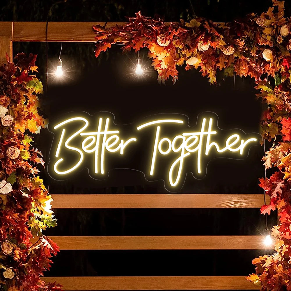 A glowing neon sign spelling Better Together framed by autumn leaves and wood planks.