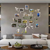 A wall collage featuring a family tree design with various framed photos and leaves on a gray wall.