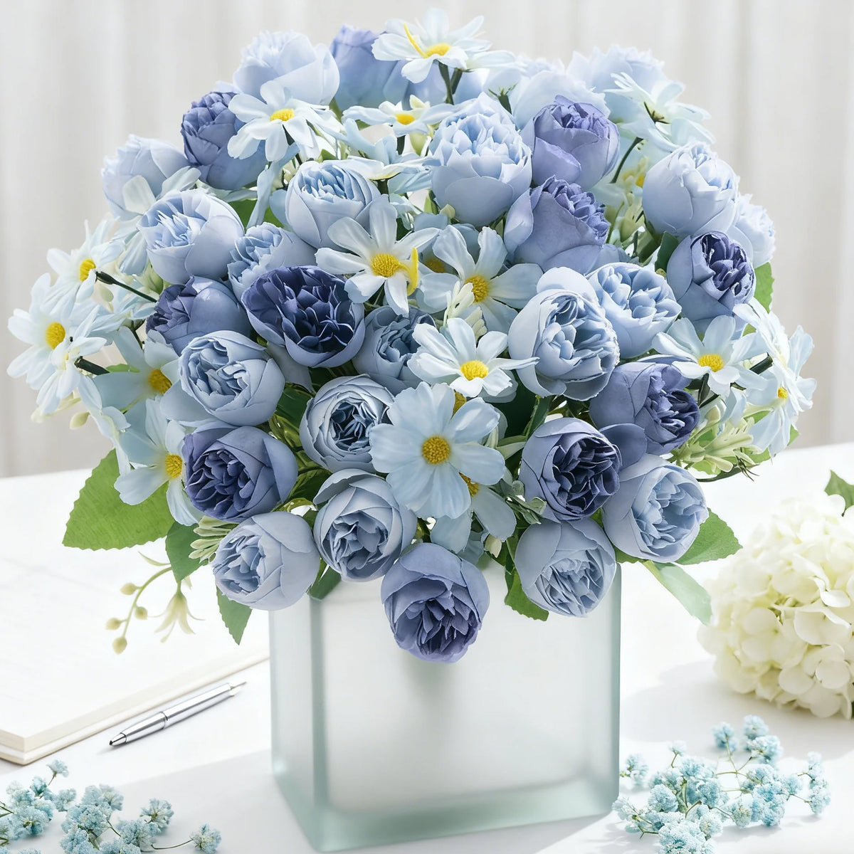 Un ramo de rosas de seda artificial en tonos azules y lavanda, arreglado en un jarrón de vidrio transparente.