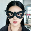 A close-up photo of a woman wearing a black cat eye masquerade mask with striking makeup and dark hair.