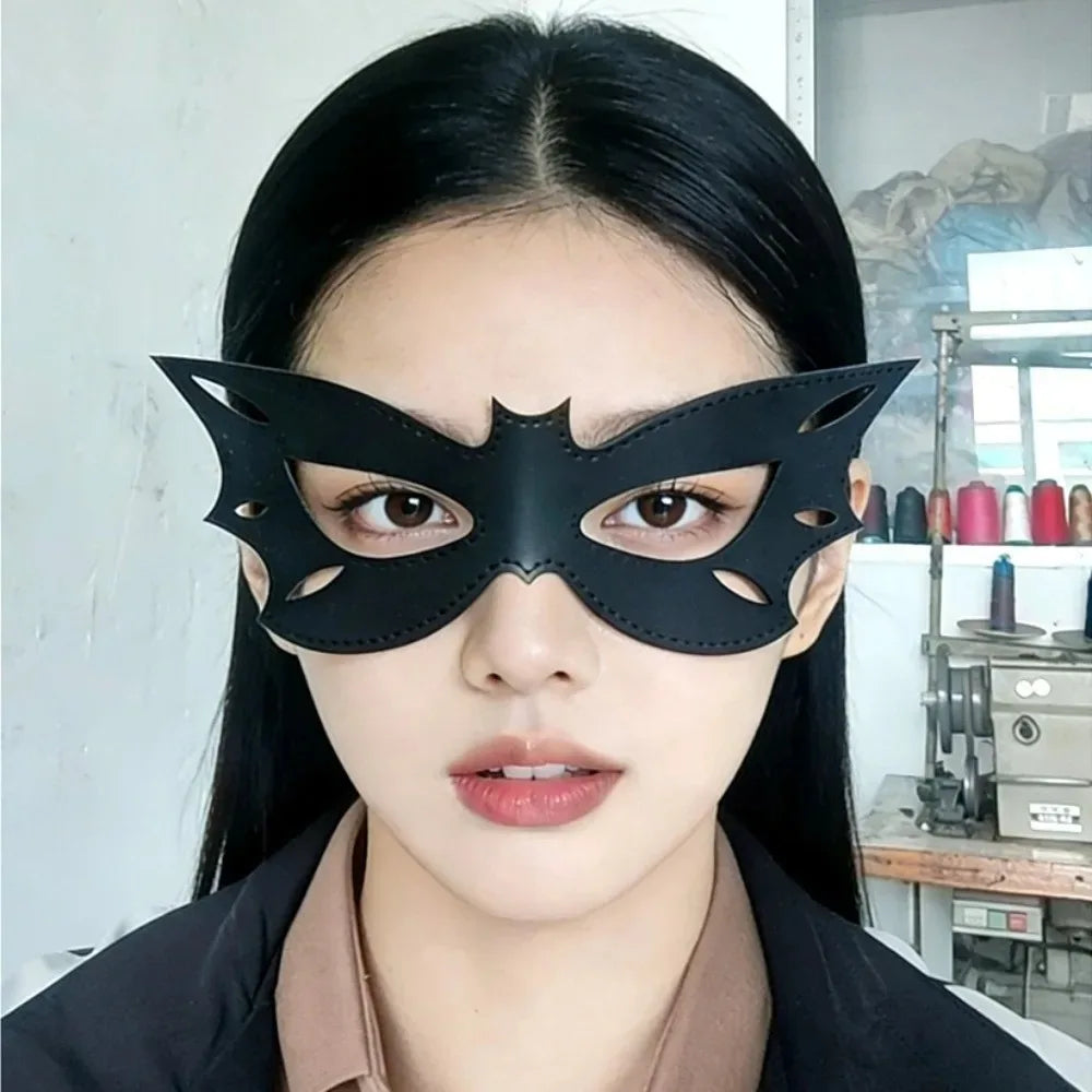 A close-up photo of a woman wearing a black cat eye masquerade mask with striking makeup and dark hair.