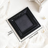 Black ornate picture frame with a dark gray mat displayed on white fabric