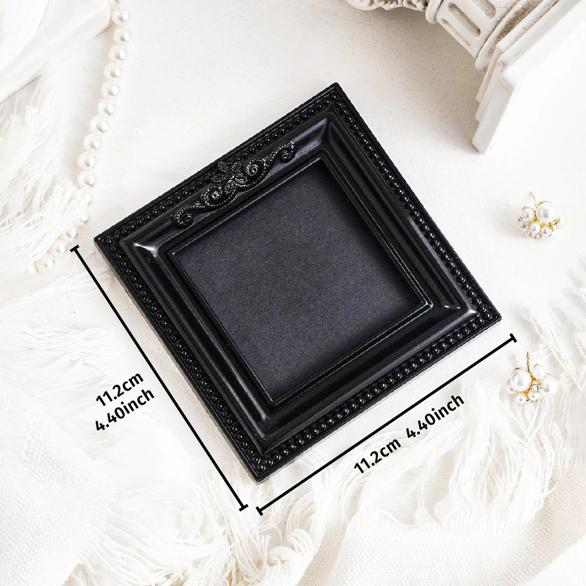 Black ornate picture frame with a dark gray mat displayed on white fabric