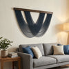 A gray sofa is positioned below a large blue macrame wall tapestry with wooden hangers.