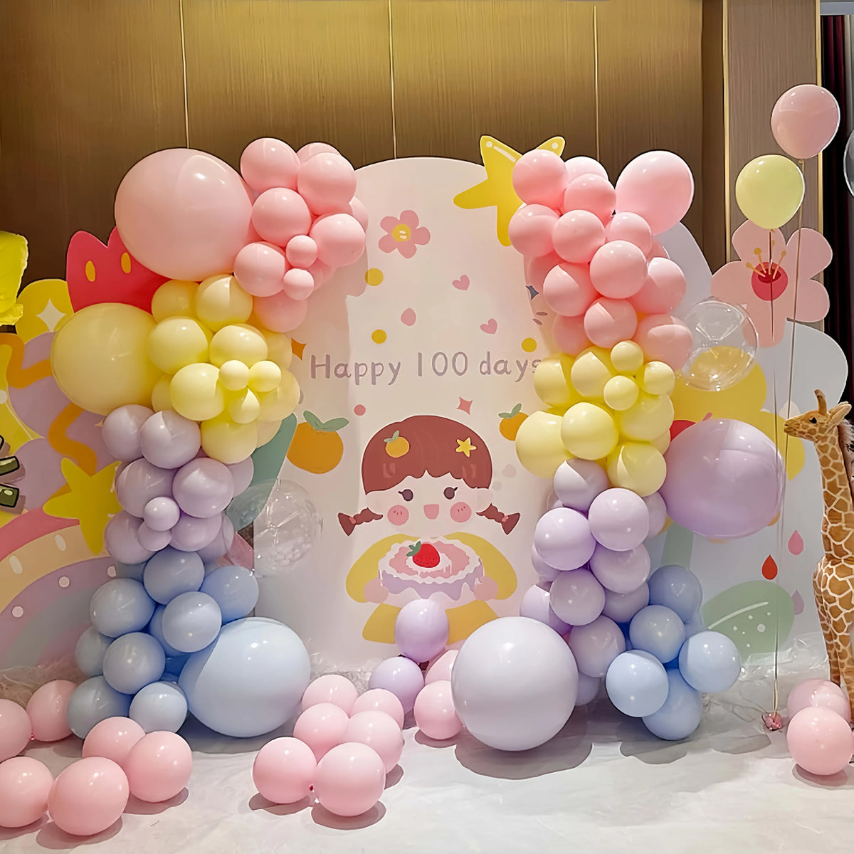 A display of pastel rainbow latex balloons in various shades of pink, yellow, and blue arranged in clusters.