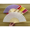 A collection of colorful silk wedding hand fans with bamboo frames arranged on a wooden surface.