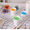 A collection of white disposable paper cups filled with various colored drinks, including orange, blue, and green.
