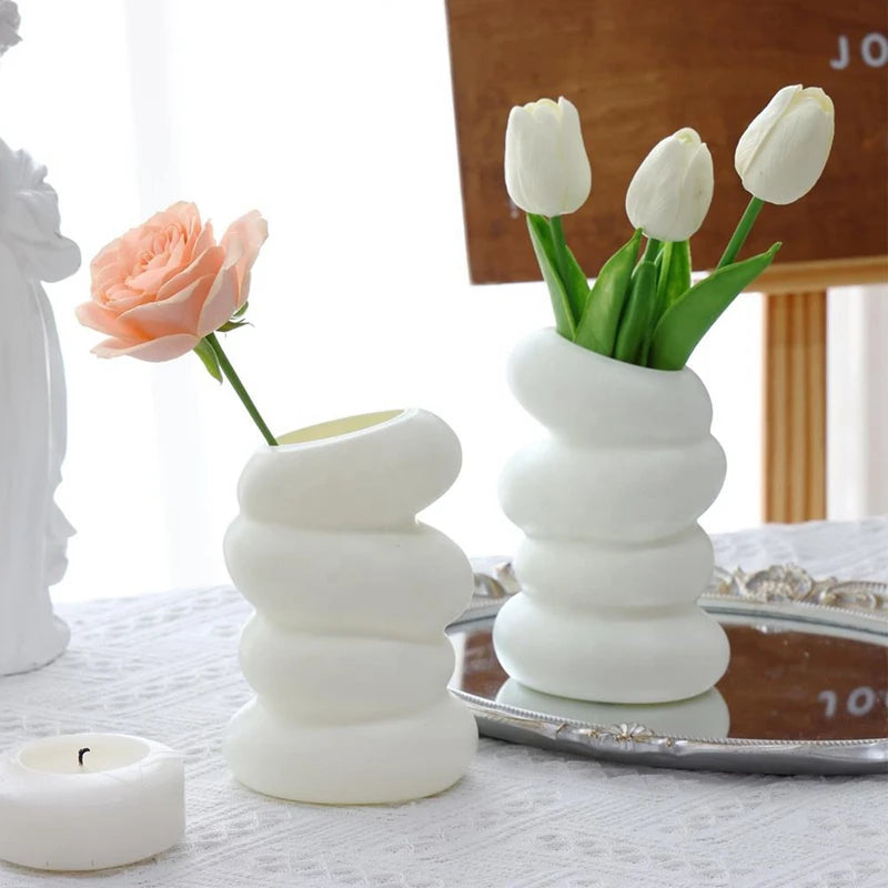 A white ceramic Nordic spiral decorative vase holding three white tulips on a silver tray.