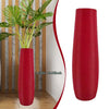 A bright red, ribbed, cylindrical floor vase is shown in a natural wood setting.