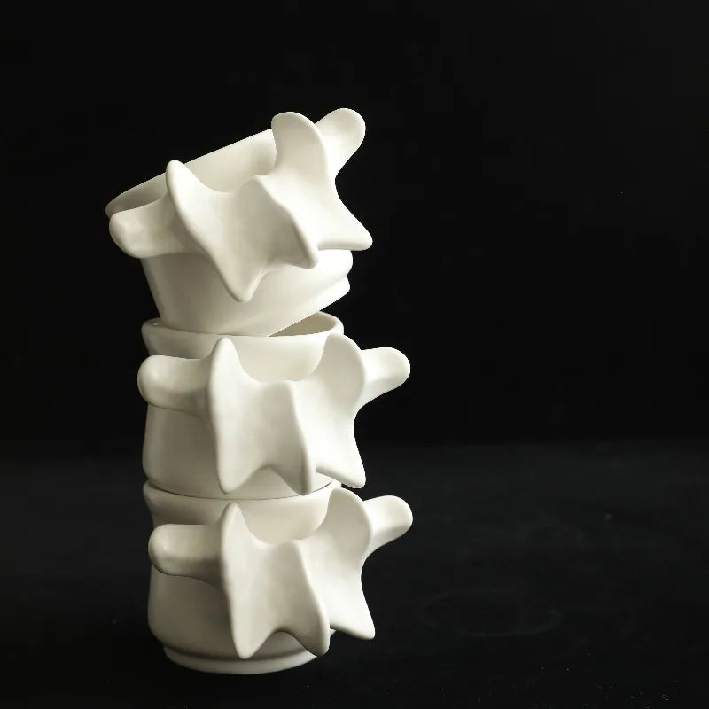 A stack of white ceramic vertebrae-shaped decorative vases against a dark background.