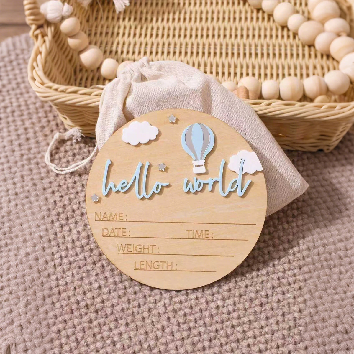 A wooden birth announcement sign with clouds and a hot air balloon design resting on a beige fabric.