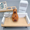 Pendentif de capybara orange sur plateau en bois à côté d'un appareil électronique blanc.