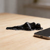 A black, draped reclining female statue sculpture rests on a light wooden desk next to a smartphone.
