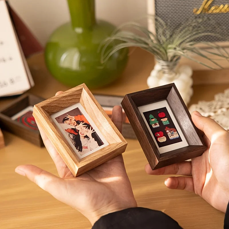 A hand holds a small wooden photo frame displaying a polaroid picture.