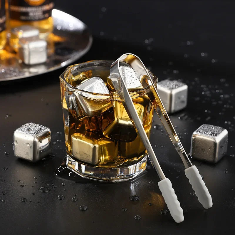 Reusable stainless steel ice cubes in a glass with a metal spoon on a dark surface