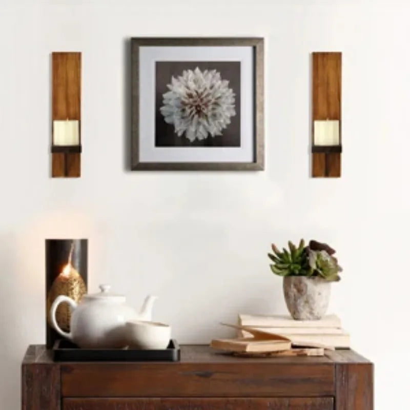 Vintage wooden wall candle holders flanking a framed floral print above a dark wooden cabinet.
