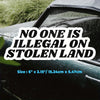 Black decal sticker with white text saying No One Is Illegal On Stolen Land placed on a dark vehicle surface.