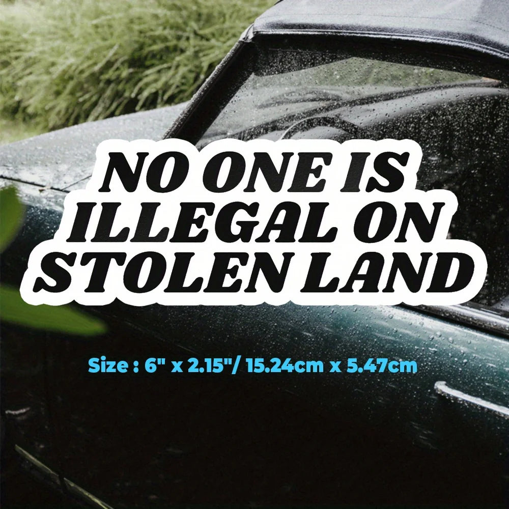 Black decal sticker with white text saying No One Is Illegal On Stolen Land placed on a dark vehicle surface.