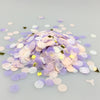A pile of multicolor paper confetti consisting of purple, pink, and gold pieces scattered on a light surface.