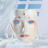 A pale, porcelain masquerade mask with intricate floral designs and delicate white ties is displayed on a white cloth.