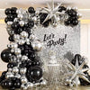 A decorative balloon arch and wreath featuring black and silver balloons against a sparkling background.