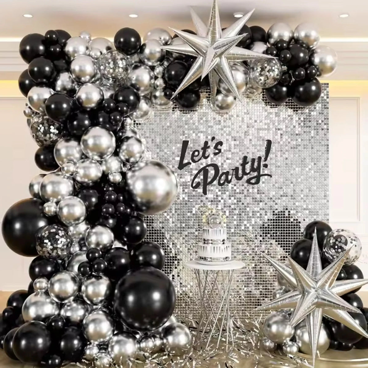 A decorative balloon arch and wreath featuring black and silver balloons against a sparkling background.