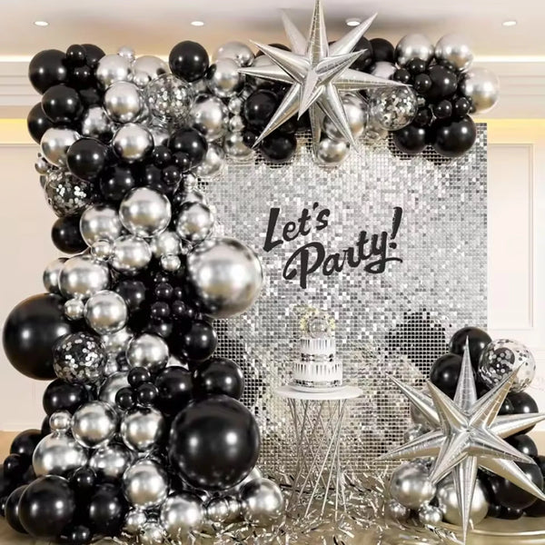 A decorative balloon arch and wreath featuring black and silver balloons against a sparkling background.
