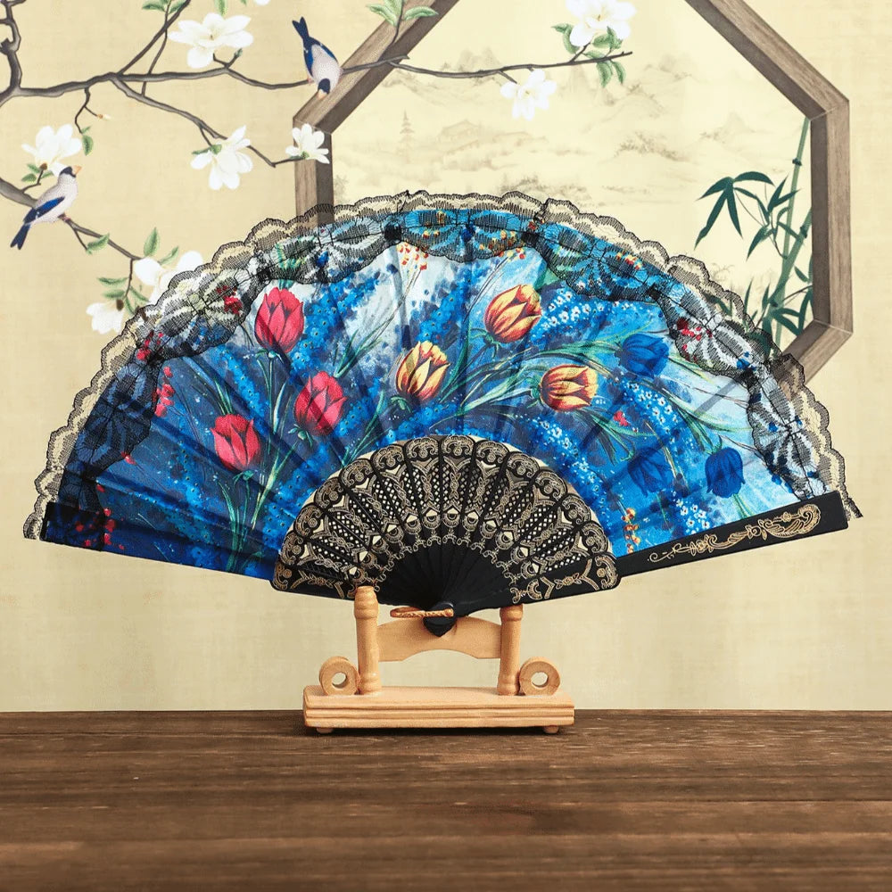 A Spanish style folding lace trim handheld fan with blue and floral patterns displayed against a light background.