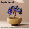 A handcrafted crystal tree with blue lapis lazuli crystals mounted on a copper wire base, resting in a light yellow bowl.
