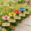 A garden decoration featuring a bee watering station with a ladder among colorful flowers and butterflies.