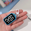 A hand holds a blue LED keychain pocket watch with a digital display showing 2:00 PM.