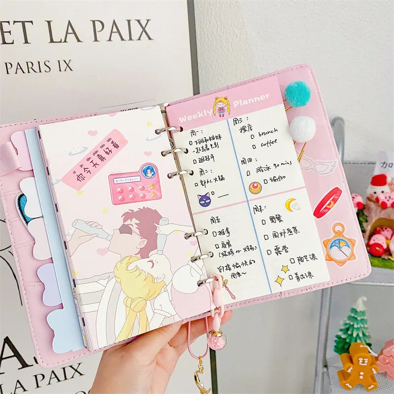 A pink planner with decorative pages and a heart pendant attached, showing weekly planning layouts.