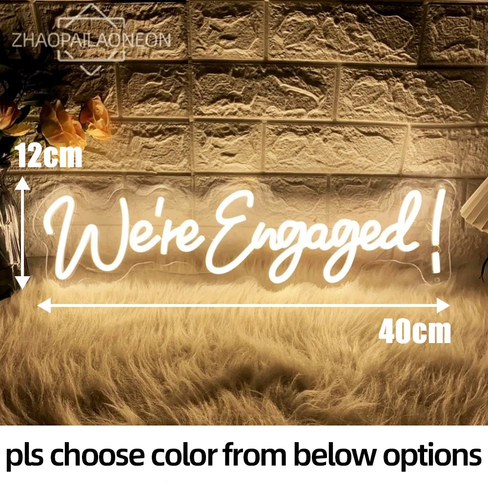 A glowing neon sign spelling 'We're Engaged!' is displayed against a textured wall with fluffy fur, showing a 40cm width and 