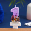 A purple glitter candle set featuring a number one and three small character figures on a white base.