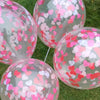 A collection of clear balloons filled with pink and red heart-shaped sequins confetti scattered on green grass.
