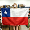 A blonde woman holds up a large tapestry of the Chilean flag featuring blue, white, and red colors.