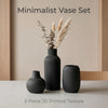 A set of three matte black ceramic vases with vertical ribbed texture displayed on a light surface.