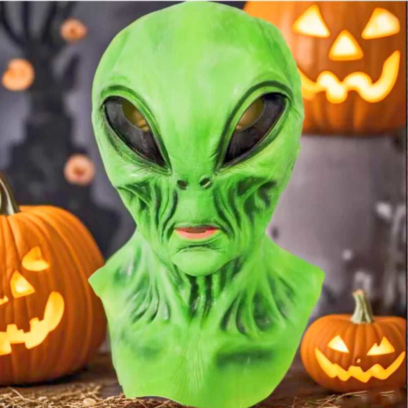 A realistic green alien full-face latex mask displayed in a Halloween context with pumpkins.
