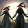 Two witches in black dresses with carved pumpkin heads standing against a glowing background.