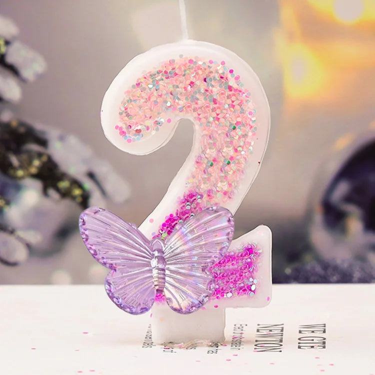A white digital candle shaped like the number 2 decorated with pink and purple glitter and a purple butterfly on a white surf